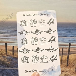 Könnte beinhalten: Eine weiße Karte mit schwarzen Strichzeichnungen eines Koffers, Flip-Flops, Palmen, einer Sonne, einem Liegestuhl und einem Flugzeug. Die Karte trägt den Text "Urlaubs-Spar-Challenge" und "Sparbetrag". Die Karte wird von einer Hand vor einem Hintergrund eines Strandes mit Sand und einem Holzzaun gehalten.
