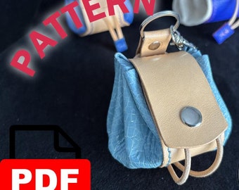 Könnte beinhalten: Ein PDF-Muster für eine kleine, blaue und braune Ledertasche mit einem silbernen Druckknopfverschluss und einem Lederriemen. Die Tasche hat einen Schlüsselring. Das Bild enthält auch den Text "PATTERN" und "HANDCRAFTED LEATHERWORK".