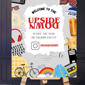 May include: A decorative sign on an easel with a gray background and various illustrations. The sign reads "Welcome to the Upside NMOO" in red and black text. It includes a bicycle, rainbow, cassette tape, and the hashtag #strangerkids011.