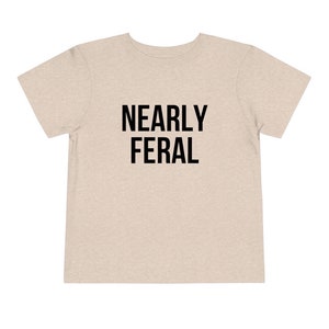 May include: A light beige t-shirt with the text "NEARLY FERAL" printed in black.