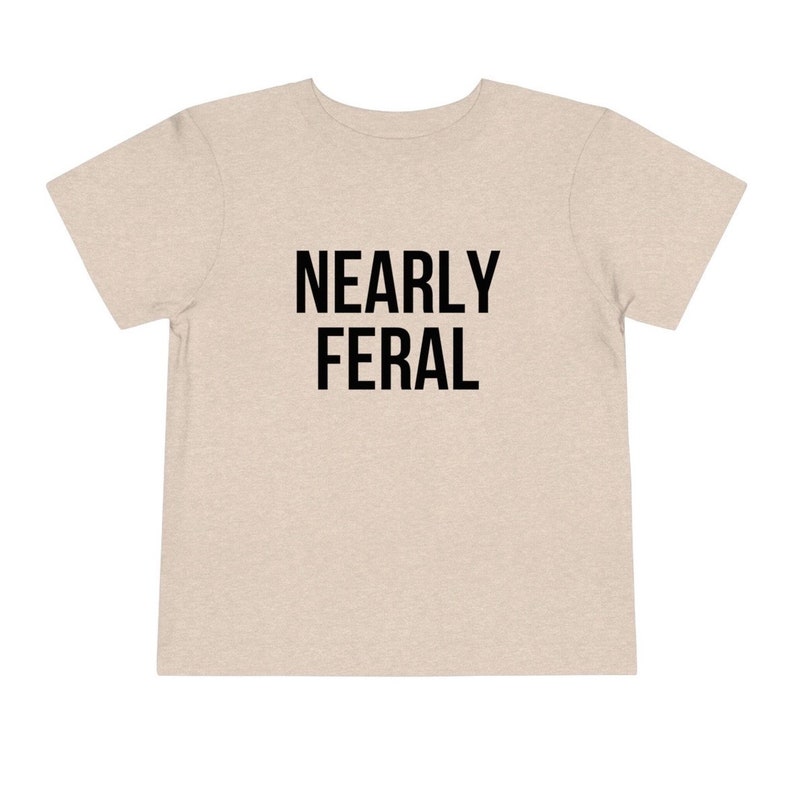 May include: A light beige t-shirt with the text "NEARLY FERAL" printed in black.