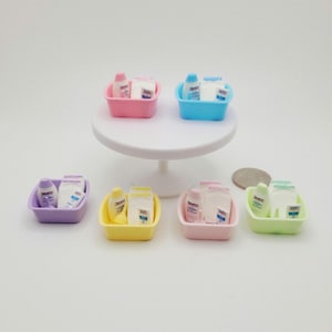 May include: Six miniature plastic basins in pastel colors, each containing tiny bottles and folded white cloths. The basins are pink, blue, purple, yellow, light pink, and light green. A white pedestal stand holds two basins, while four sit below.