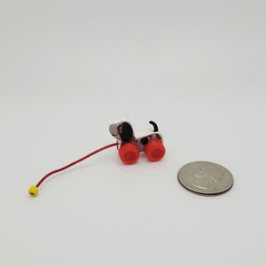 May include: A miniature pull-along toy dog with a white body, black spots, and red wheels. The dog has a red pull string with a yellow ball at the end. A U.S. quarter is next to the toy.
