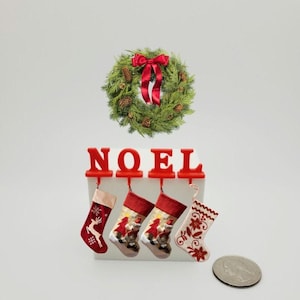 May include: Red NOEL stocking holder with four stockings hanging from it. The stockings are decorated with Christmas themes. A green Christmas wreath with a red bow is above the holder.