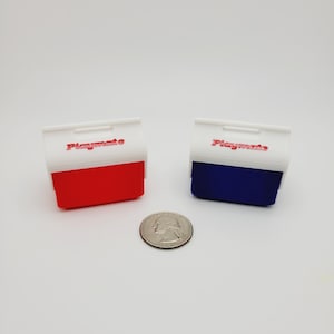 May include: Two small, rectangular Playmate coolers, one red and one blue, with white lids and red text. A quarter is placed between the coolers. The coolers are approximately 3 inches wide and 2 inches tall.