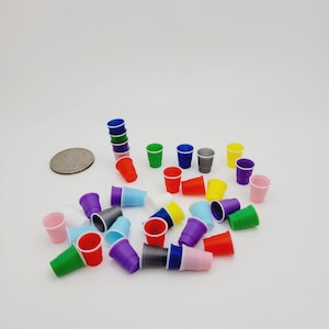 May include: A collection of miniature plastic cups in various colors including red, blue, green, yellow, purple, pink, white, and grey. The small cups are scattered across the surface, with one stack of four cups and a silver coin for scale.