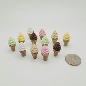 May include: A collection of miniature ice cream cones with various pastel-colored soft serve, including white, pink, green, yellow, and brown. The cones are a light brown color. A coin is in the lower right corner.