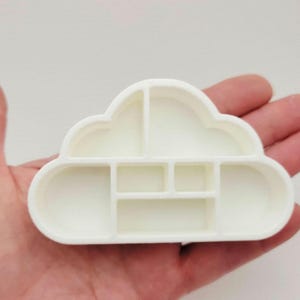 May include: A white cloud-shaped cookie cutter with a multi-sectioned interior design. The frame is constructed with a continuous outer wall and several internal dividers that create distinct compartments within the cloud shape.