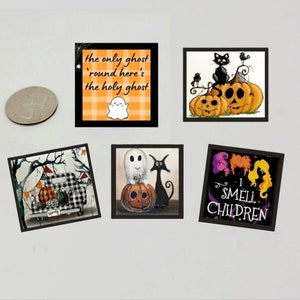 May include: Five small, square Halloween-themed art prints in black frames. The prints feature a ghost, pumpkins, a black cat, and the text "I SMELL CHILDREN" and "the only ghost 'round here's the holy ghost".