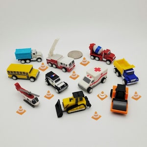 May include: A collection of colorful toy vehicles, including a school bus, fire truck, ambulance, and cement mixer. The toys are arranged with small orange traffic cones on a white surface. A coin is also present.
