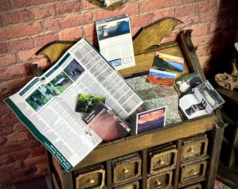 May include: A miniature wooden cabinet filled with Great Smoky Mountains National Park brochures, maps, and postcards. The cabinet has multiple small drawers and a decorative top. A brick wall serves as the backdrop.
