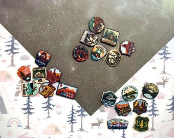 May include: A collection of small, multi-shaped patches featuring colorful illustrations of various United States national parks, including Arches, Grand Canyon, Olympic, Zion, and Lake Tahoe, with text labels identifying each specific location.