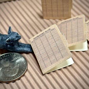 May include: Three brown paper folders with gridded pages and the text "Index Document Number" on the front. The folders are stacked on top of each other and are sitting on a brown corrugated cardboard surface.