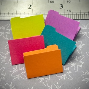 May include: Five colorful file folders in different colors: yellow, pink, teal, orange, and red. The folders are arranged in a stack with the top folder being yellow and the bottom folder being red.