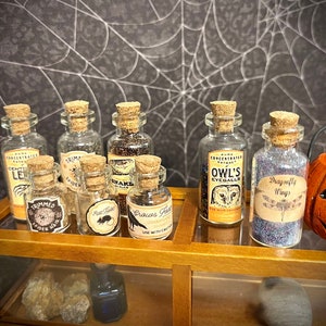 May include: Ten small glass bottles with cork stoppers and labels. The bottles are filled with various liquids and have labels with text such as "Trimmed Spider Hair", "Craves Eyes", "Owl's Eyeballs", and "Dragonfly Wings".
