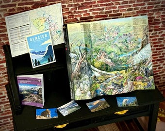 May include: A black desk displays a map, brochures, and postcards featuring Glacier National Park. The map shows colorful geographical details. Postcards showcase mountain landscapes and wildlife. The word "GLACIER" is visible on a brochure.
