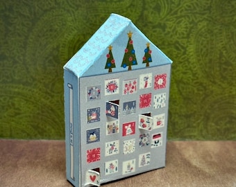 May include: A blue paper house shaped advent calendar with 24 small doors, each with a different Christmas-themed illustration. The doors are partially open, revealing a red heart behind one of the doors. The top of the house has three small Christmas trees with red and gold ornaments.