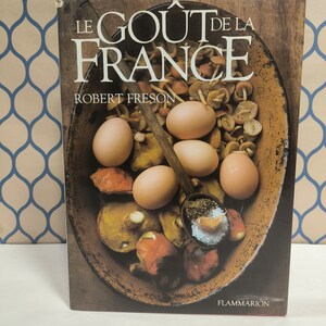 Op de afbeelding: Een kookboek getiteld "Le Gout de la France" van Robert Freson, met een bruine houten kaft en een foto van een kom met champignons en eieren.