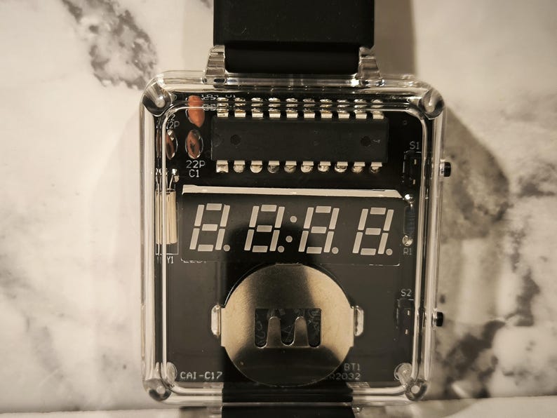 K&ouml;nnte beinhalten: Eine transparente, quadratische Digitaluhr mit schwarzem Zifferblatt, das die Zeit "8:8:8:8" anzeigt. Die Uhr hat ein schwarzes Armband und sichtbare interne Komponenten. Das Uhrengeh&auml;use ist transparent und gibt den Blick auf die Platine und andere elektronische Elemente frei.