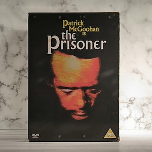 May include: DVD case cover featuring a black and white image of Patrick McGoohan as "The Prisoner". The text on the cover reads "Patrick McGoohan is The Prisoner".