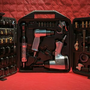 以下が含まれることがあります： レンチ、ハンマー、ネイルガンなど、さまざまなエアーツールが入った黒いケースが開いています。ツールはグリッドパターンで配置されており、すべてシルバーです。
