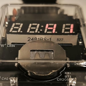 K&ouml;nnte beinhalten: Nahaufnahme eines elektronischen Ger&auml;ts aus klarem Kunststoff mit einer Digitalanzeige, die die Zahlen 18:18:18 anzeigt. Die Anzeige ist rot. Das Ger&auml;t hat ein silbernes Metallteil und eine Leiterplatte.