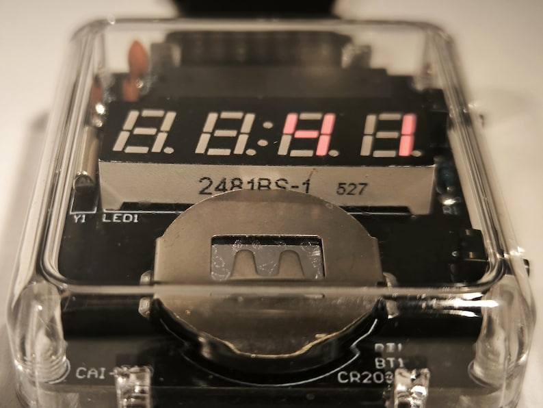 K&ouml;nnte beinhalten: Nahaufnahme eines elektronischen Ger&auml;ts aus klarem Kunststoff mit einer Digitalanzeige, die die Zahlen 18:18:18 anzeigt. Die Anzeige ist rot. Das Ger&auml;t hat ein silbernes Metallteil und eine Leiterplatte.