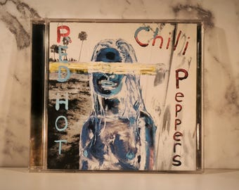 Puede incluir: Caja de CD con la portada del álbum Red Hot Chili Peppers. La obra de arte representa una figura en tonos azules con una barra amarilla que oscurece los ojos. El nombre de la banda y el título del álbum están escritos en rojo y azul.