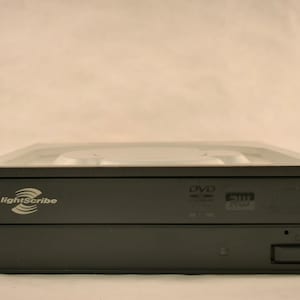 Peut inclure: Un lecteur de DVD externe noir avec un logo LightScribe argenté et une étiquette de DVD qui indique "DVD-ROM 16X MAX".