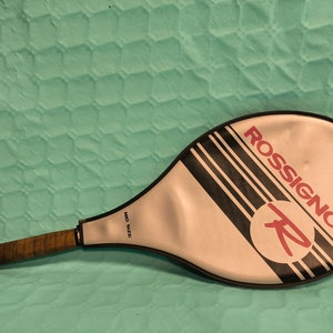 May include: A white and black tennis racket with the word "ROSSIGNOL" in red letters on the face. The racket is labelled "MID SIZE".