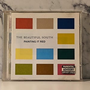 Puede incluir: Una caja de CD con el álbum "Painting It Red" de The Beautiful South. La portada muestra una cuadrícula de cuadrados de colores: rojo, beige, azul marino, amarillo, amarillo claro, azul, verde oscuro, oliva, marrón y una pegatina de Parental Advisory.