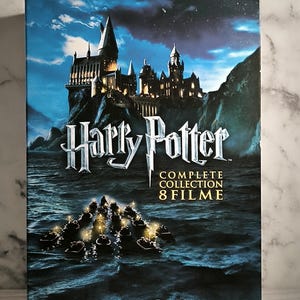Può includere: Un cofanetto DVD della collezione completa dei film di Harry Potter. La scatola presenta un'immagine notturna del castello di Hogwarts su una scogliera che domina un'oscura distesa d'acqua. Il testo sulla scatola recita "Harry Potter Collezione Completa 8 Film 8 Dischi DVD".