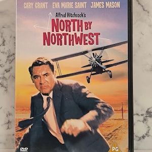 Puede incluir: Carátula de DVD para la película "Con la muerte en los talones" dirigida por Alfred Hitchcock. La carátula presenta a Cary Grant, Eva Marie Saint y James Mason. La película está clasificada como PG.