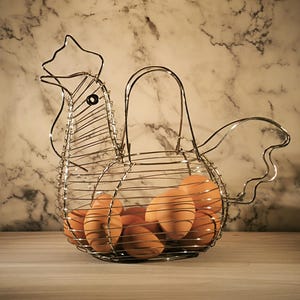 May include: A wire rooster-shaped egg basket filled with brown eggs. The basket is made of silver-colored wire and has a handle. The eggs are a light brown color. The background is a marble-patterned wall.