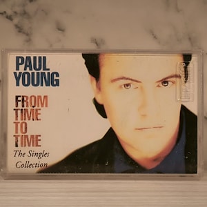 Puede incluir: Una caja de cassette con una foto de Paul Young en la portada. El título del álbum es "From Time To Time: The Singles Collection."