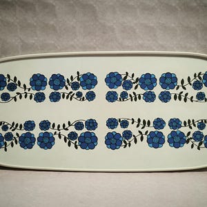 May include: Rectangular serving tray with a white background and a floral pattern. The design features blue flowers and black stems arranged in symmetrical rows. The tray has rounded corners and a white border.