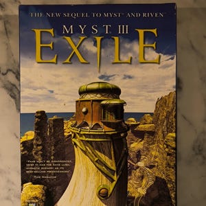 Peut inclure: Une boîte de jeu vidéo rectangulaire pour Myst III Exile représentant une haute tour de forme organique et de couleur claire sur un paysage rocheux sous un ciel bleu. Le titre est imprimé en grandes lettres jaunes avec la marque Ubi Soft.