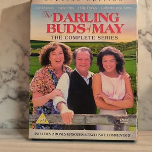 Pode incluir: Caixa de DVD da sitcom britânica "The Darling Buds of May" com David Jason, Pam Ferris, Philip Franks e Catherine Zeta-Jones. A caixa inclui a série completa e dois episódios bônus. A imagem mostra os atores em pé em frente a um campo verde.