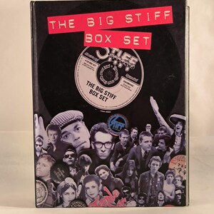 Könnte beinhalten: Ein schwarzes und weißes Box-Set mit einem roten Titel, der "The Big Stiff Box Set" lautet. Das Box-Set zeigt eine Collage aus Schwarzweißfotos von Musikern und ein schwarzes und weißes Plattenlabel mit dem Text "Stiff Records" in Weiß.