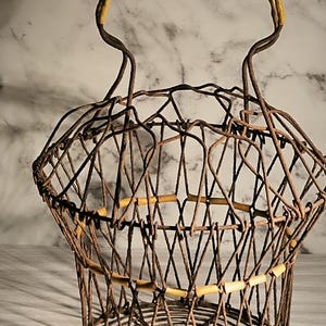 May include: An antique wire basket with a yellow handle. The basket is made of brown metal wires woven together in a diamond pattern. The rim of the basket has small wooden accents.