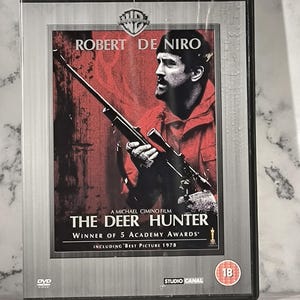 Puede incluir: Caja de DVD de "The Deer Hunter" con Robert De Niro. La portada muestra a De Niro con un rifle, el título de la película y los premios. Parte de "The Essential War Collection" de Studio Canal.