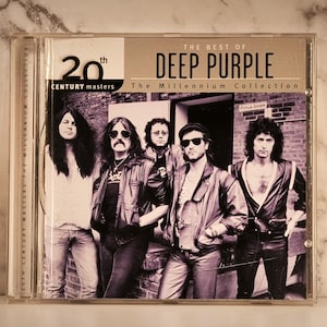 Peut inclure: Un boîtier de CD avec l'album "The Best of Deep Purple: The Millennium Collection." La couverture présente une photo en noir et blanc des membres du groupe. Le texte "20th Century Masters" est également visible.