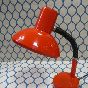 May include: A bright orange desk lamp with a flexible arm and a round base. The lamp has a simple design and is made of metal.