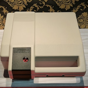 May include: A beige plastic case with a black latch and a red button. The case has a label that says "SEIMITSU".