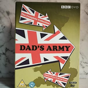 Pode incluir: Conjunto de DVD de "Dad's Army: The Complete Collection". A capa apresenta o título em letras vermelhas grandes com um design de seta Union Jack. O logotipo da BBC DVD está no topo e o conjunto inclui 14 discos.