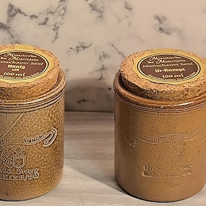 May include: Two brown ceramic jars with cork lids. The lids have gold labels with black text that reads "Moutarde be Montjole Monschauer Senf" and "Honig" or "Ur-Rezept". The jars are 100 ml each.