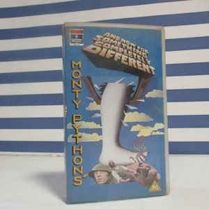 Peut inclure: Une cassette VHS du film "Monty Python's And Now For Something Completely Different". La couverture présente un pied géant avec un homme et un porcelet en dessous. L'arrière-plan est bleu avec des nuages blancs.