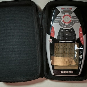 May include: A black zipped case contains a PowerBrain Sudoku game. The console is grey, black, and red, with a screen showing a Sudoku puzzle. The console has buttons labelled "Enter", "Sound", "Hint/Solve", and "Legal".