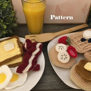 Puede incluir: Dos platos de comida de desayuno de ganchillo. Un plato tiene dos rebanadas de tostadas, dos huevos y una tira de tocino. El otro plato tiene un waffle, un panqueque, un plátano y fresas. La palabra "Pattern" está escrita en un marco blanco en el fondo.