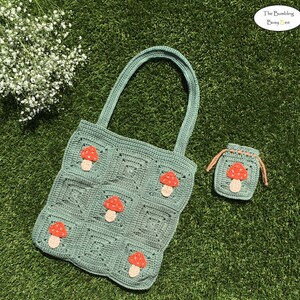 May include: A crocheted tote bag and matching drawstring pouch in a soft green color. Each item features appliqued mushrooms with red caps and beige stems. The bag has a square design, and the pouch has a drawstring closure. The Bumble Bee logo is in the top right corner.